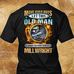Op de afbeelding: Zwart t-shirt met de tekst "MOVE OVER BOYS LET THIS OLD MAN SHOW YOU HOW TO BE A MILLWRIGHT." Het ontwerp bevat een cirkelvormige afbeelding van een machinist aan het werk, omringd door vlammen en sterren.