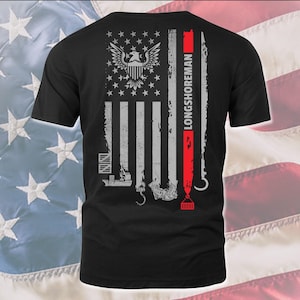 May include: Black t-shirt featuring a graphic of an American flag with a bald eagle and the text "LONGSHOREMAN" on the right side. The flag is distressed and has a crane hook and a container ship at the bottom.