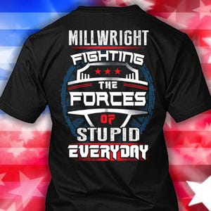 Puede incluir: Camiseta negra con el texto "MILLWRIGHT FIGHTING THE FORCES OF STUPID EVERYDAY" en letras blancas y rojas. El diseño incluye un gráfico azul y rojo con estrellas.