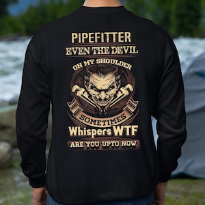May include: Black sweatshirt with a graphic design on the back. The design features a devil face with the text "PIPEFITTER EVEN THE DEVIL ON MY SHOULDER SOMETIMES WHISPERS WTF ARE YOU UPTO NOW."