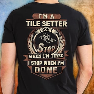 Może przedstawiać: Czarna koszulka z napisem "I'M A TILE SETTER I DON'T STOP WHEN I'M TIRED I STOP WHEN I'M DONE". Projekt zawiera kielnię i grafikę płytek, z brązowym i beżowym schematem kolorów.