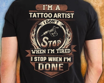 Może przedstawiać: Czarna koszulka z napisem "I'M A TATTOO ARTIST I DON'T STOP WHEN I'M TIRED I STOP WHEN I'M DONE". Projekt zawiera maszynkę do tatuażu i elementy dekoracyjne w odcieniach brązu i beżu.