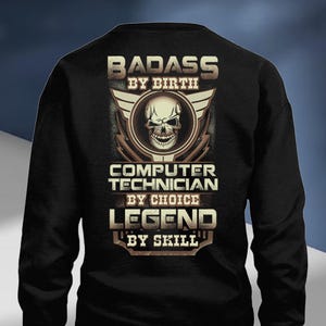 May include: Black sweatshirt with a graphic design. The design features a skull in a circular emblem with the words "BADASS BY BIRTH", "COMPUTER TECHNICIAN BY CHOICE", and "LEGEND BY SKILL" in a bold, stylized font.