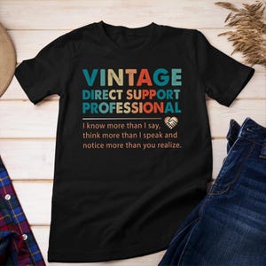 May include: Black t-shirt with a vintage-style design that says "Vintage Direct Support Professional". The text is in a rainbow colour scheme. Below the text is a quote that says "I know more than I say, think more than I speak and notice more than you realize."