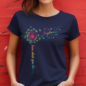 Puede incluir: Camiseta azul marino con un diseño de diente de león colorido. Las palabras "love what you do" y "Longshoreman" están escritas en una fuente caprichosa. El diente de león tiene acentos rosas, amarillos, verdes y azules.