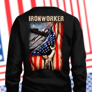 May include: Black sweatshirt featuring an American flag design with a hand holding the flag. The image includes the text "IRONWORKER" at the top. The design also depicts ironworkers on a steel beam.
