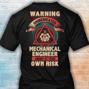 Könnte beinhalten: Ein schwarzes T-Shirt mit einem Grafikdesign und dem Text WARNING UNMEDICATED MECHANICAL ENGINEER ANNOY AT YOUR OWN RISK. Das Design enthält ein rotes Dreieck, ein Zahnrad und ein Zirkelsymbol in einem kreisförmigen Rahmen mit orangefarbenen und roten Akzenten.