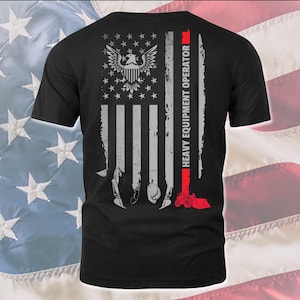 May include: Black t-shirt with a distressed American flag design. The flag has a bald eagle in the top left corner and the words "Heavy Equipment Operator" in red on the right side.