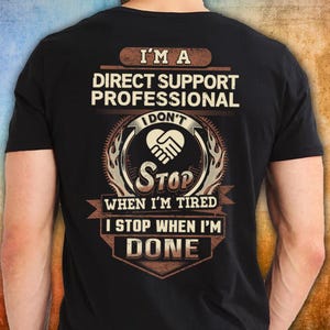 May include: Black t-shirt featuring the text "I'M A DIRECT SUPPORT PROFESSIONAL I DON'T STOP WHEN I'M TIRED I STOP WHEN I'M DONE." The design includes a handshake graphic and flame-like accents.