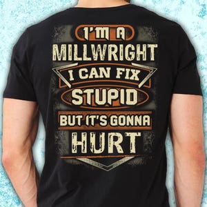 Op de afbeelding: Zwart T-shirt met de tekst "I'M A MILLWRIGHT I CAN FIX STUPID BUT IT'S GONNA HURT" in witte en oranje letters. Het ontwerp heeft een verweerde, vintage uitstraling.