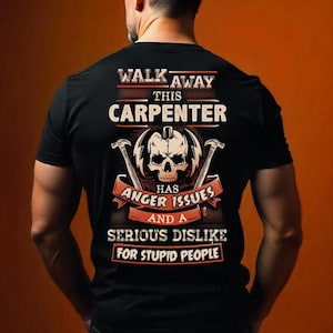 May include: Black t-shirt with a graphic design featuring a skull, hammers, and text. The text reads "WALK AWAY THIS CARPENTER HAS ANGER ISSUES AND A SERIOUS DISLIKE FOR STUPID PEOPLE."