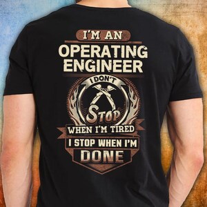 May include: Black t-shirt featuring the text "I'M AN OPERATING ENGINEER I DON'T STOP WHEN I'M TIRED I STOP WHEN I'M DONE". The design includes a circular emblem with crossed tools and flame accents.