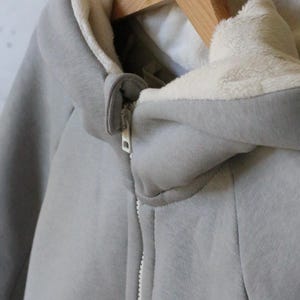 May include: A gray hooded sweatshirt with a white fleece lining. The zipper is white and the sweatshirt has a relaxed fit.