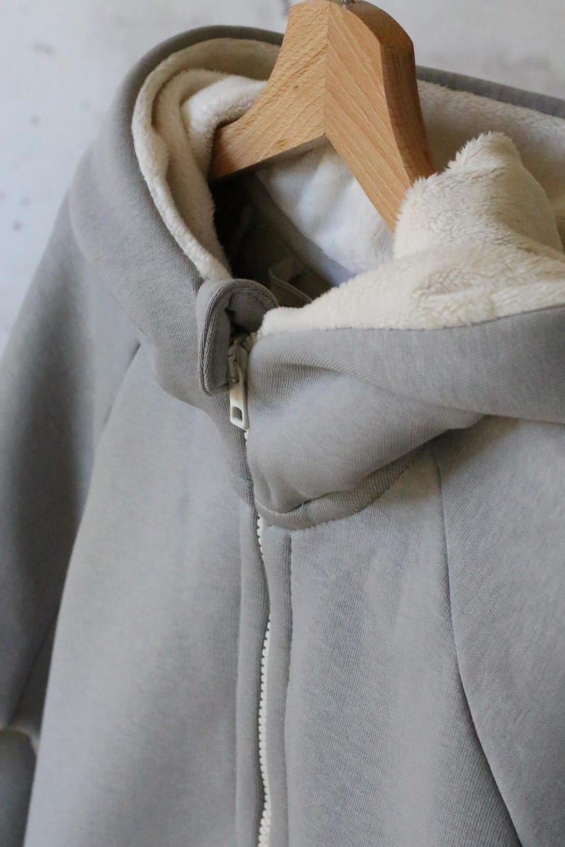 May include: A gray hooded sweatshirt with a white fleece lining. The zipper is white and the sweatshirt has a relaxed fit.