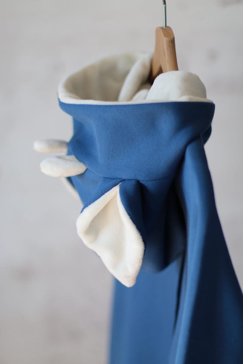 K&ouml;nnte beinhalten: Ein blauer Kapuzenpullover mit wei&szlig;em Fleece-Futter und Ohren an der Kapuze.