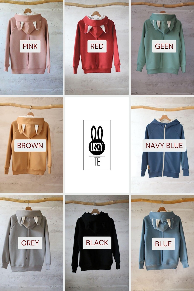 May include: Nine different color hooded sweatshirts with bunny ears on the hood. The colors are pink, red, green, brown, navy blue, grey, black, and blue. The sweatshirts are hanging on wooden hangers.
