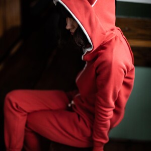 May include: A red hooded sweatshirt with white ears and a white trim around the hood. The sweatshirt is made of a soft, comfortable material.
