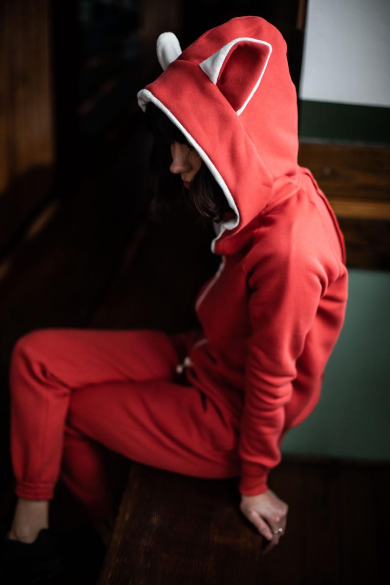 May include: A red hooded sweatshirt with white ears and a white trim around the hood. The sweatshirt is made of a soft, comfortable material.