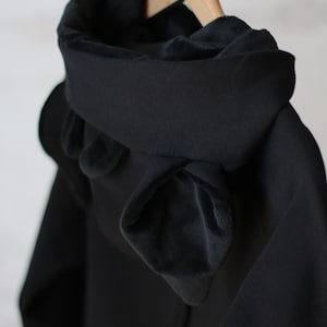 K&ouml;nnte beinhalten: Schwarze Kapuzenjacke mit weichem, pl&uuml;schigen Futter. Die Kapuze ist heruntergeklappt und hat ein einzigartiges, geschichtetes Design.