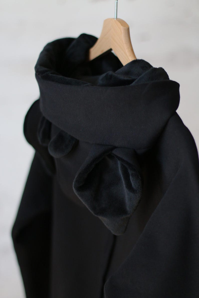 K&ouml;nnte beinhalten: Schwarze Kapuzenjacke mit weichem, pl&uuml;schigen Futter. Die Kapuze ist heruntergeklappt und hat ein einzigartiges, geschichtetes Design.