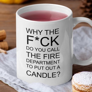 Puede incluir: Taza de cerámica blanca con una cita humorística en texto negro: "WHY THE F*CK DO YOU CALL THE FIRE DEPARTMENT TO PUT OUT A CANDLE?" La taza está llena de un líquido rosa. El fondo incluye palitos de canela, un pastel y una servilleta de lino.
