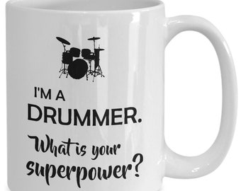 Op de afbeelding: Witte keramische mok met een zwart silhouet van een drumstel en de tekst "I'M A DRUMMER. What is your superpower?" in het zwart. De mok heeft een gebogen handvat.