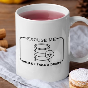 Könnte beinhalten: Weiße Keramiktasse mit dem Text "EXCUSE ME WHILE I TAKE A DUMP!" in Schwarz. Die Tasse zeigt eine Grafik eines Datenbankservers mit einem Pfeil nach unten. Die Tasse ist mit einer rosa Flüssigkeit gefüllt.