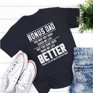 May include: A navy blue t-shirt with white text that reads "Bonus Dad... You may not have given me life but you sure have made my life better. Thanks for putting up with my mom."