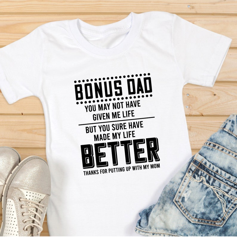 May include: White t-shirt with black text that reads "Bonus Dad You may not have given me life but you sure have made my life better Thanks for putting up with my mom."