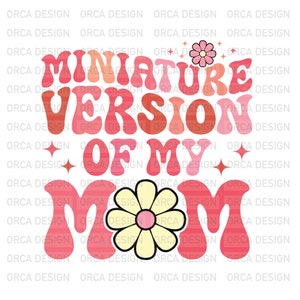 以下が含まれることがあります： レトロなフォントで「Miniature Version of My Mom」というテキストが書かれたピンクと赤のグラフィックデザイン。デザインには、黄色い中心を持つピンクの花が2つ含まれています。