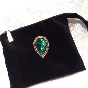 May include: A black velvet pouch with a zipper closure and a green and gold jeweled embellishment in the shape of a teardrop.