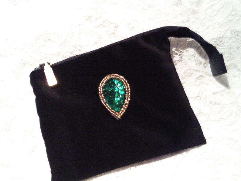 May include: A black velvet pouch with a zipper closure and a green and gold jeweled embellishment in the shape of a teardrop.