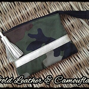 May include: A camouflage fabric pouch with a gold leather trim and a white tassel. The pouch has a zipper closure and a black strap.