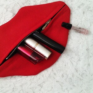May include: A red felt zippered pouch shaped like a pair of lips, open to reveal a lipstick, a lip gloss, a mascara, and a small bottle of perfume.