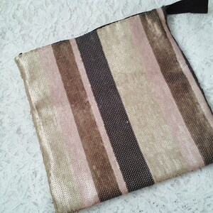 May include: A striped clutch bag with a zipper closure. The bag is made of a fabric with a metallic sheen and features alternating stripes of pink, brown, and black.