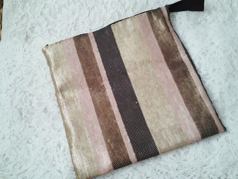 May include: A striped clutch bag with a zipper closure. The bag is made of a fabric with a metallic sheen and features alternating stripes of pink, brown, and black.