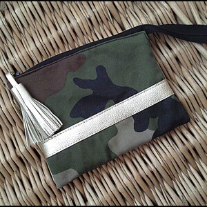 May include: A camouflage fabric pouch with a gold zipper and a gold leather trim. The pouch has a black tassel.