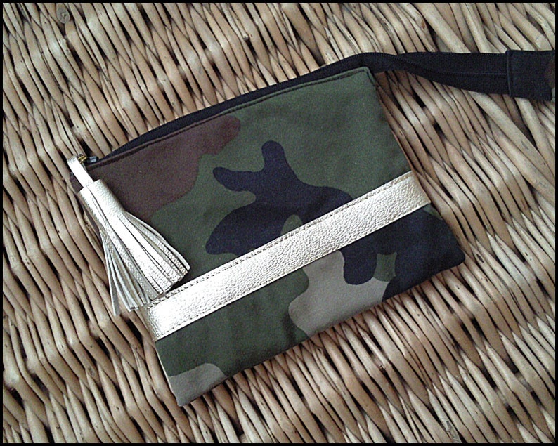 May include: A camouflage fabric pouch with a gold zipper and a gold leather trim. The pouch has a black tassel.