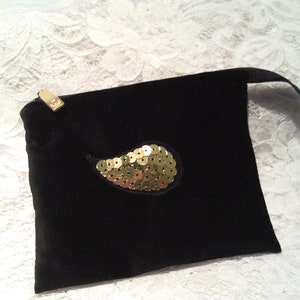 May include: A black velvet pouch with a gold sequined paisley design. The pouch has a drawstring closure and a small gold tag.