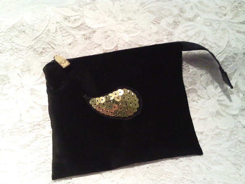 May include: A black velvet pouch with a gold sequined paisley design. The pouch has a drawstring closure and a small gold tag.