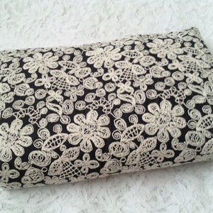 Op de afbeelding: Zwarte clutch met een wit kantpatroon. De tas heeft een ritssluiting en een klein handvat.