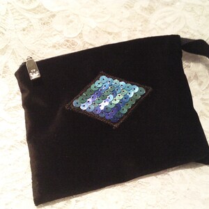 May include: A black velvet pouch with a zipper closure and a diamond-shaped design made of blue and green sequins.