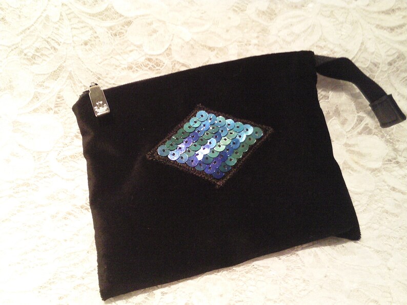 May include: A black velvet pouch with a zipper closure and a diamond-shaped design made of blue and green sequins.