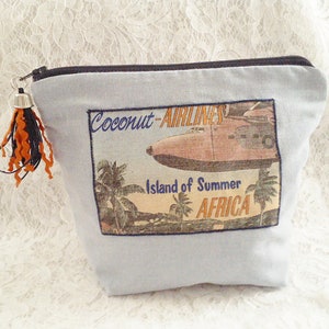 Op de afbeelding: Blauwe canvas toilettas met een vintage reisposterontwerp met een vliegtuig, palmbomen en de tekst "Coconut Airlines, Island of Summer, Africa".