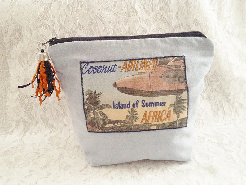 Op de afbeelding: Blauwe canvas toilettas met een vintage reisposterontwerp met een vliegtuig, palmbomen en de tekst "Coconut Airlines, Island of Summer, Africa".