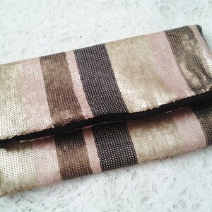 May include: A striped clutch purse with a black fabric lining. The purse is made of sequins in shades of pink, gold, and brown.