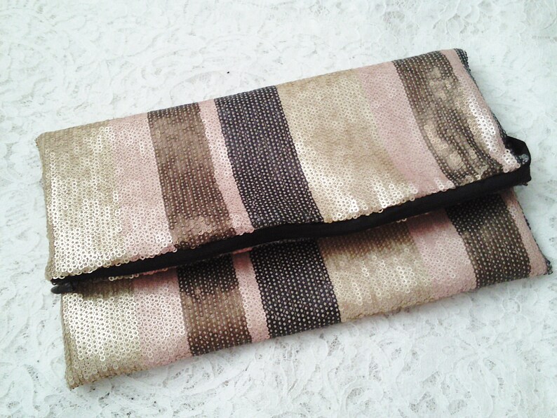 May include: A striped clutch purse with a black fabric lining. The purse is made of sequins in shades of pink, gold, and brown.