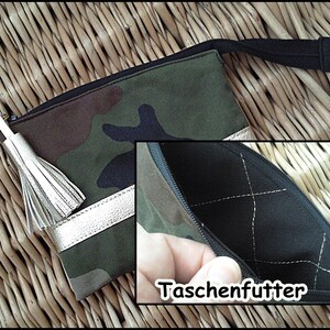 May include: A camouflage fabric pouch with a silver trim and a white tassel. The pouch has a black zipper and a black lining with a diamond pattern. The text "Taschenfutter" is visible on the lining.