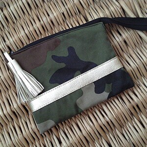 May include: A small green, brown, and black camouflage fabric pouch with a gold leather trim and a gold tassel. The pouch has a black zipper and a black strap.