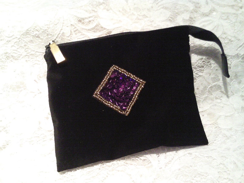May include: A black velvet pouch with a gold zipper and a purple sequined diamond-shaped embellishment.